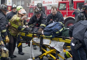 Firefighters and emergency medical personnel rush a firefighter from the scene of a multi-alarm fire at a four-story brownstone in the Back Bay neighborhood near the Charles River, Wednesday, March 26, 2014, in Boston. (AP Photo/Scott Eisen)