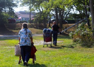 CCB MEDIA A 66-year-old Harwich native walks out of the woods, as, ahead of her, Barnstable Police Chief Paul MacDonald wheels out her belongings in a shopping cart.