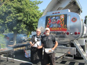 PAMELA BRIMMER PHOTO Former Chief of Police Michael Whelan (left) and Ken Foster, owner of Hall Oil, flip donated franks and burgers behind the big X-Grill at National Night Out in Dennis Port in 2014.